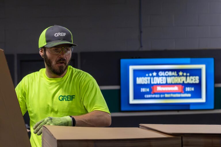 A Greif colleague works hard in the foreground as a most loved workplaces banner displays in the background